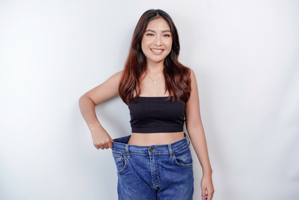 Diet and weight loss concept. A young Asian woman in oversized jeans.