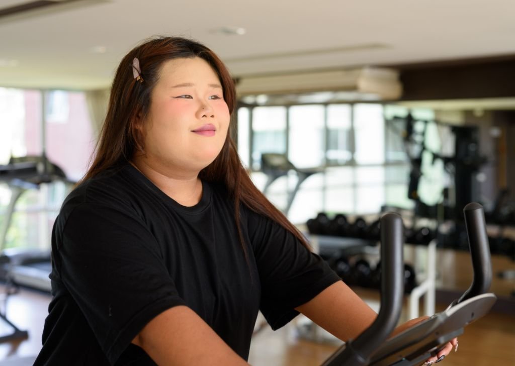 An obese woman exercising on a cycling machine.